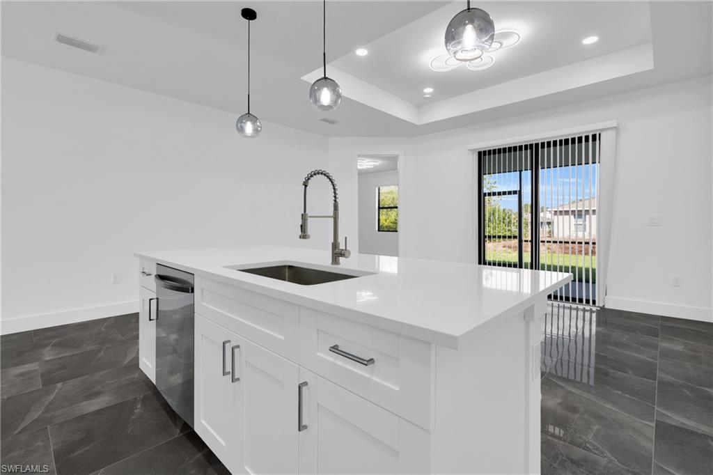 Kitchen with white cabinets, a center island with sink, decorative light fixtures, light stone counters, and dishwasher
