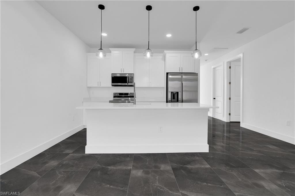 Kitchen with stainless steel appliances, white cabinetry, an island with sink, and pendant lighting