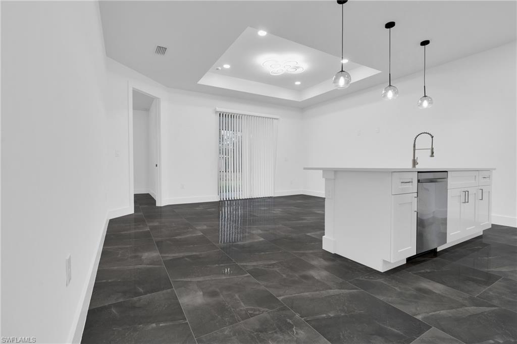 Kitchen with hanging light fixtures, a raised ceiling, an island with sink, white cabinets, and stainless steel dishwasher