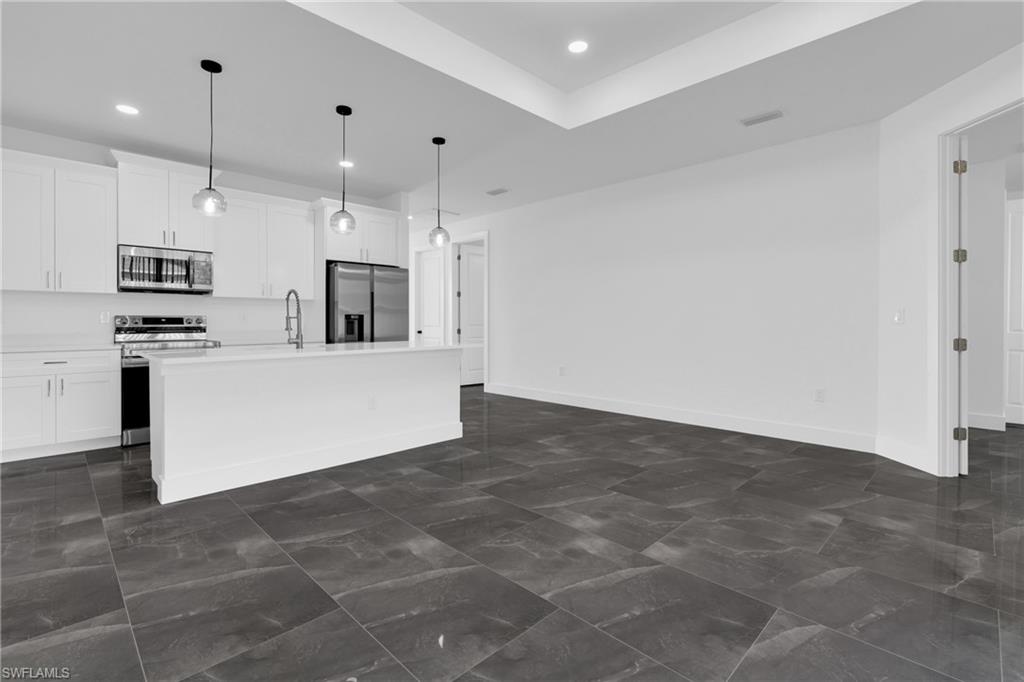 Kitchen with stainless steel appliances, white cabinetry, a center island with sink, pendant lighting, and a raised ceiling