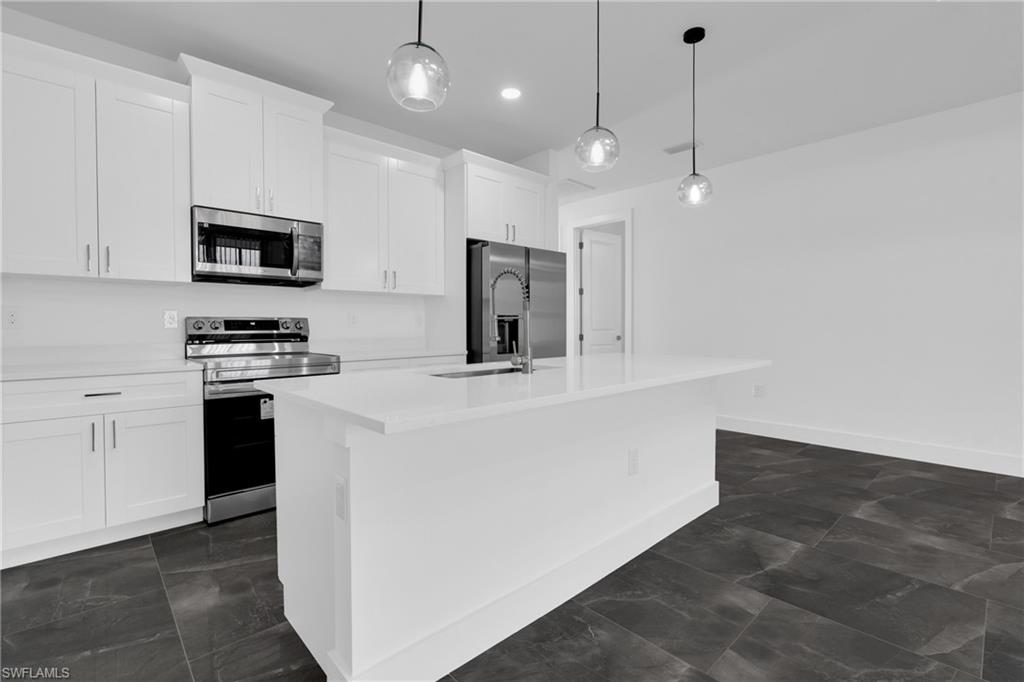 Kitchen with stainless steel appliances, white cabinetry, hanging light fixtures, a kitchen island with sink, and light stone countertops