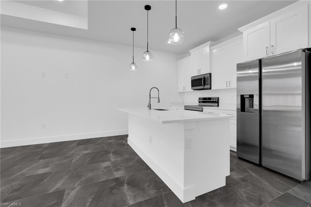 Kitchen with stainless steel appliances, white cabinets, an island with sink, pendant lighting, and light stone counters