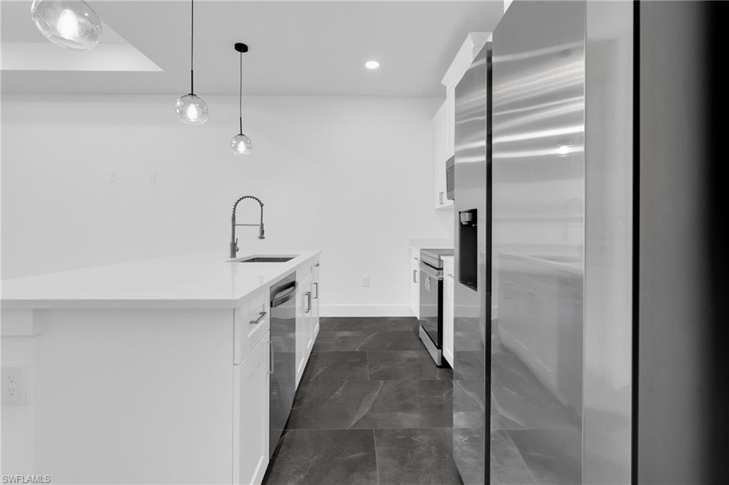 Kitchen with stainless steel appliances, white cabinets, light stone counters, decorative light fixtures, and a kitchen island with sink