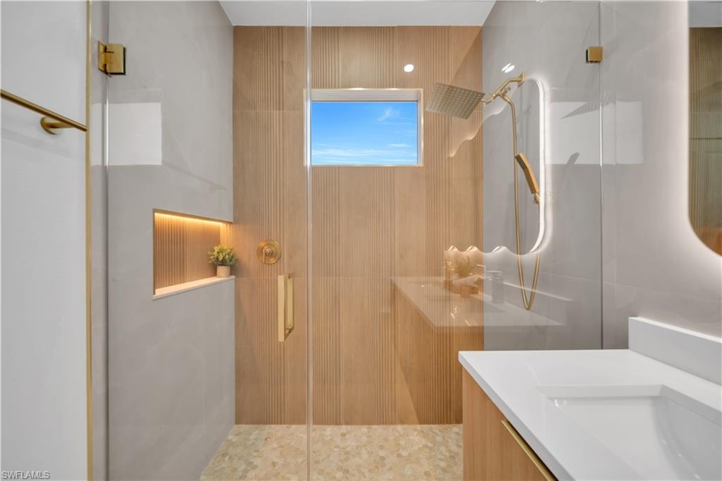 Glass-enclosed shower with gold-tone fixtures, wood-finish wall paneling, and an illuminated recessed niche