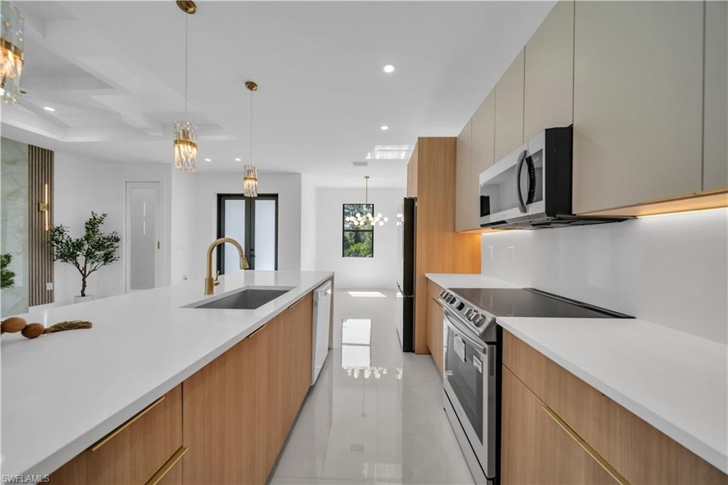 Kitchen featuring an elongated island with an undermount sink, brass faucet, and white countertops