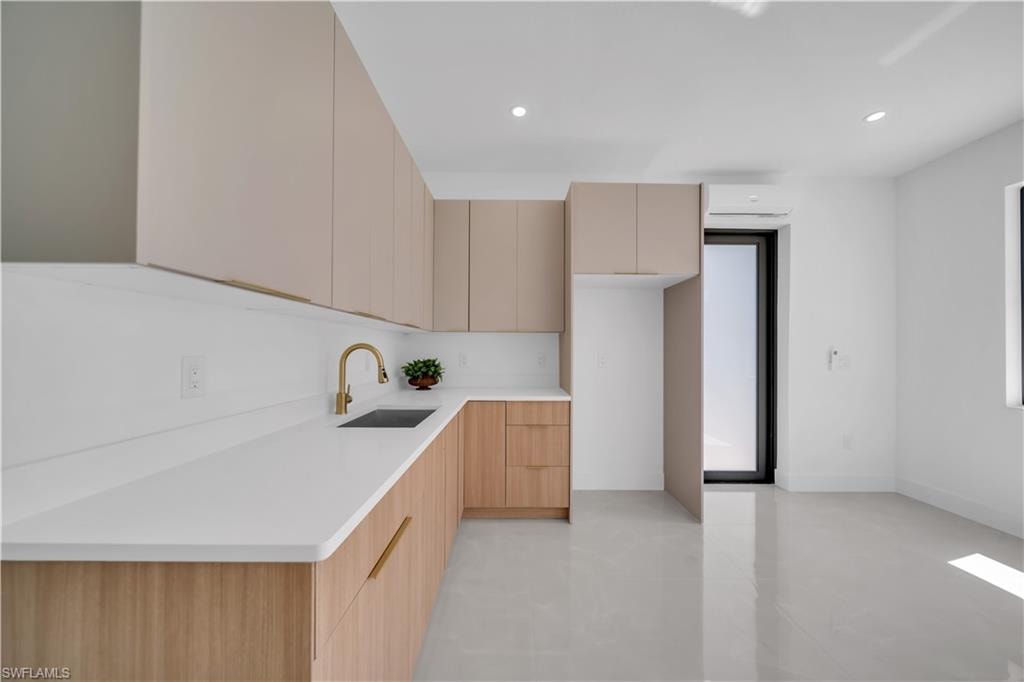 Modern kitchen featuring light wood-finish lower cabinetry, matte beige upper cabinetry, white countertops, and a gold-finish faucet