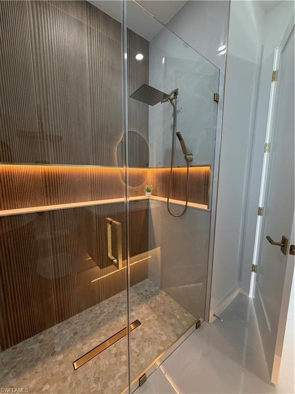 Glass-enclosed shower featuring a rainfall showerhead, handheld shower, pebble-style flooring, and a linear drain