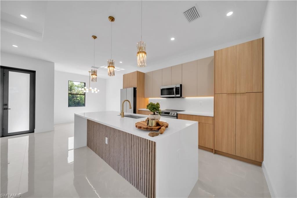 Spacious kitchen featuring an expansive central island with a waterfall countertop, integrated sink, and gold-finish faucet