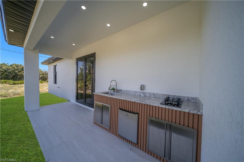 Covered patio featuring an outdoor kitchen with a built-in cooktop, stainless steel sink, and light-toned countertop
