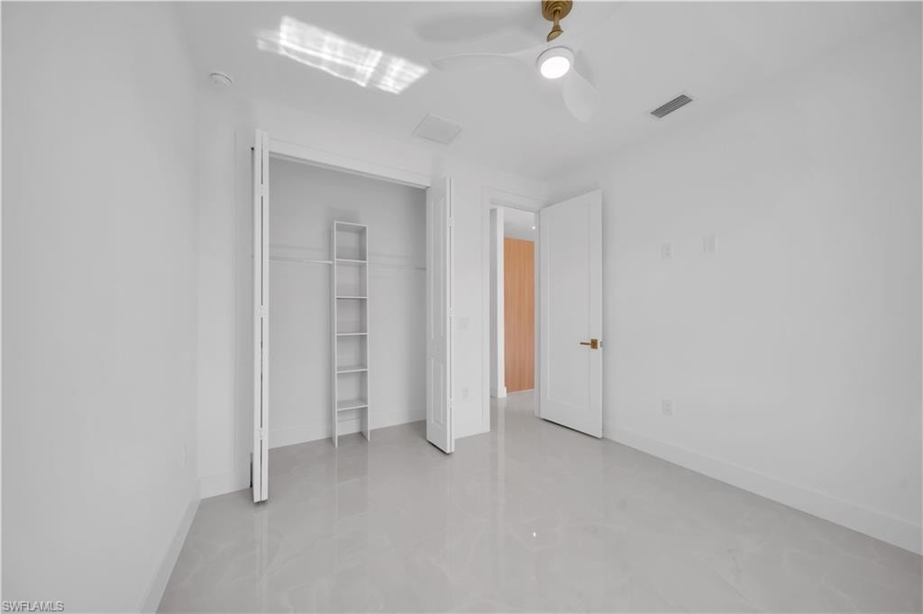 White walls, light-toned flooring, bifold closet doors, built-in shelving, ceiling fan with integrated lighting