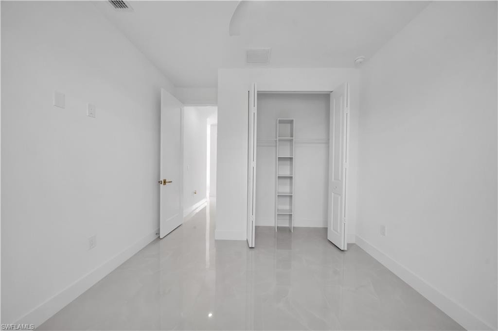 White walls with a smooth finish, light-toned tile flooring, and a closet featuring built-in shelving