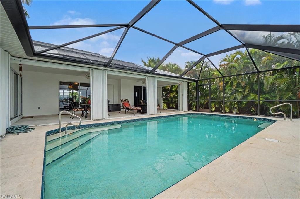 Screened-in pool and patio with a covered outdoor living area, featuring a tiled pool interior, concrete decking, and mature tropical landscaping