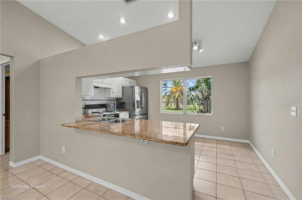 Kitchen pass-through with a stone-finish countertop, white cabinetry, stainless steel appliances, and tile flooring
