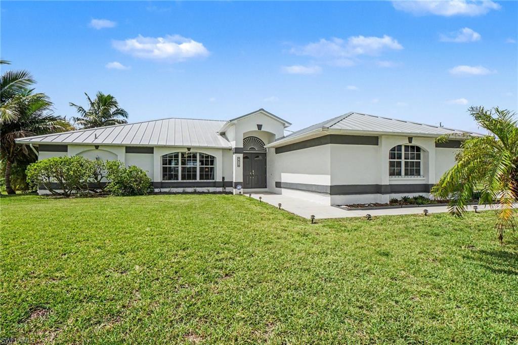 Modern single-story residence featuring a metal roof, stucco exterior, arched window details, and a paved walkway with ground lighting