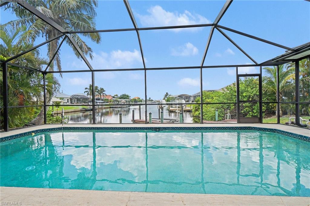 Screened outdoor swimming pool with a patterned tile border and light-colored deck
