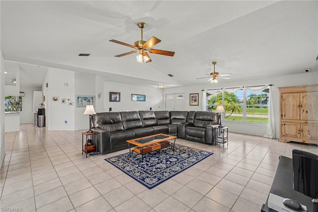 Spacious living area featuring tiled flooring, vaulted ceilings, and multiple ceiling fans