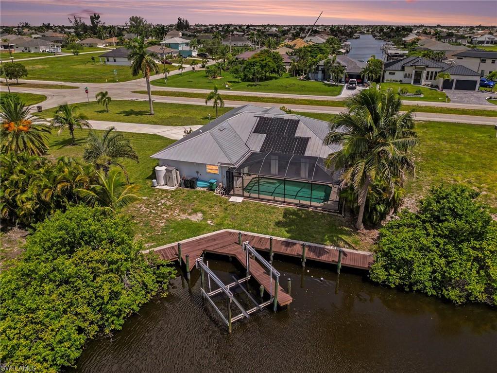 Canal-front residence featuring a private boat dock, in-ground swimming pool with screen enclosure, solar panels, and a gabled roof