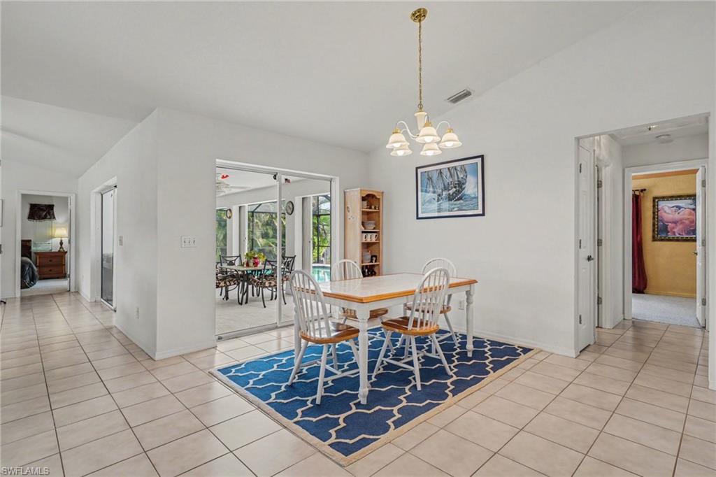 Vaulted ceiling with an attached chandelier, ceramic tile flooring, and sliding glass doors opening to an enclosed patio