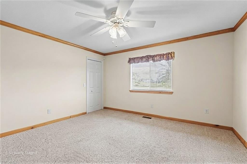 Ceiling fan light fixture, carpet flooring, wall-mounted window, wood trim, and a white interior door