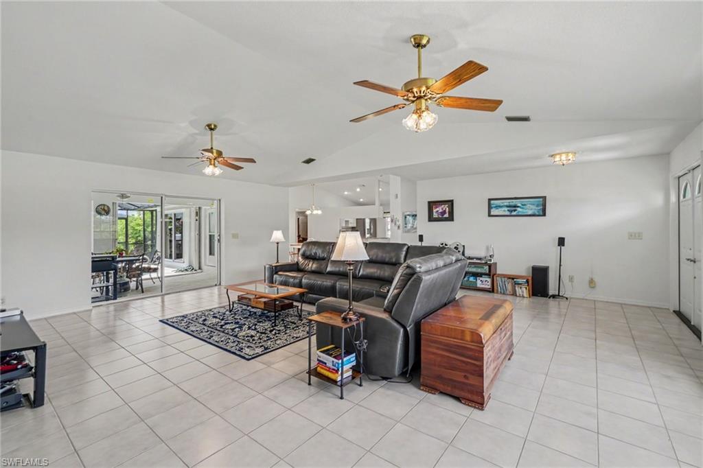 Spacious living area featuring tile flooring, vaulted ceilings, dual ceiling fans, and sliding glass doors leading to an enclosed patio