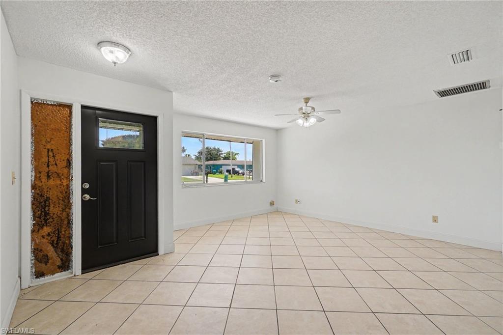 Tile flooring, white walls, ceiling fan, and a front entry door with a sidelight