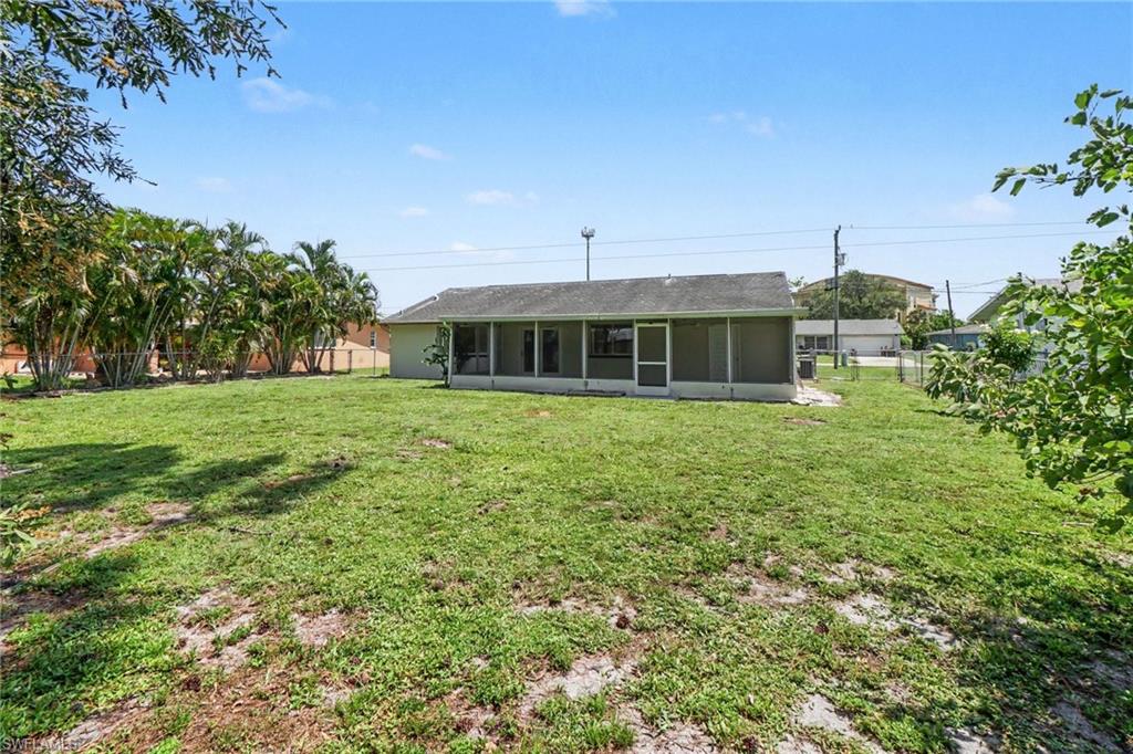 Expansive backyard with a screened porch, mature palm trees, and a chain-link fence
