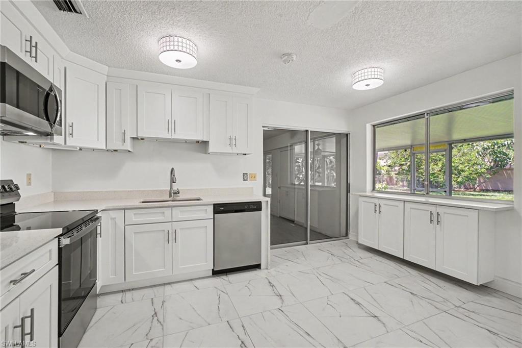 White shaker-style cabinetry with matte black hardware, stainless steel appliances, stone countertops, large format marble-look tile flooring, and sliding glass doors
