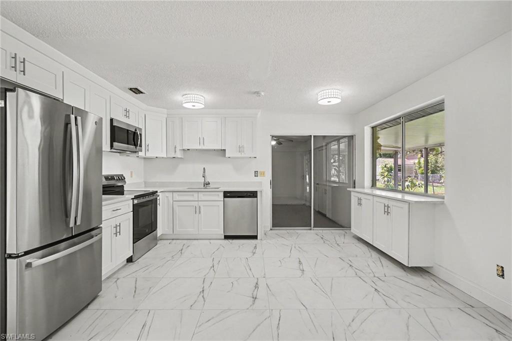 Kitchen featuring white cabinetry, stainless steel appliances, white countertops, and large format tile flooring