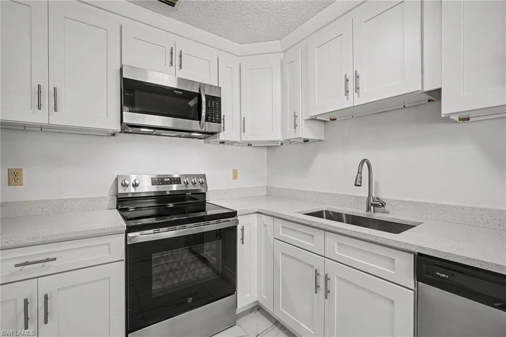 Kitchen featuring white shaker cabinetry, stainless steel appliances, light-toned countertops, and a stainless steel sink with a pull-down faucet