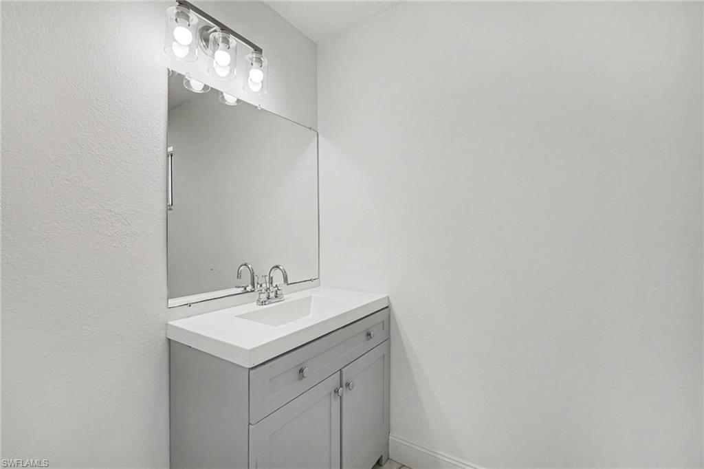 Vanity with integrated sink, chrome faucet, wall-mounted mirror, and overhead lighting fixture