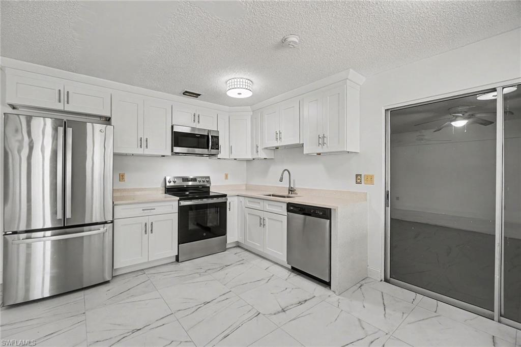 Contemporary kitchen featuring white cabinetry, stainless steel appliances, light countertops, and large format tile flooring