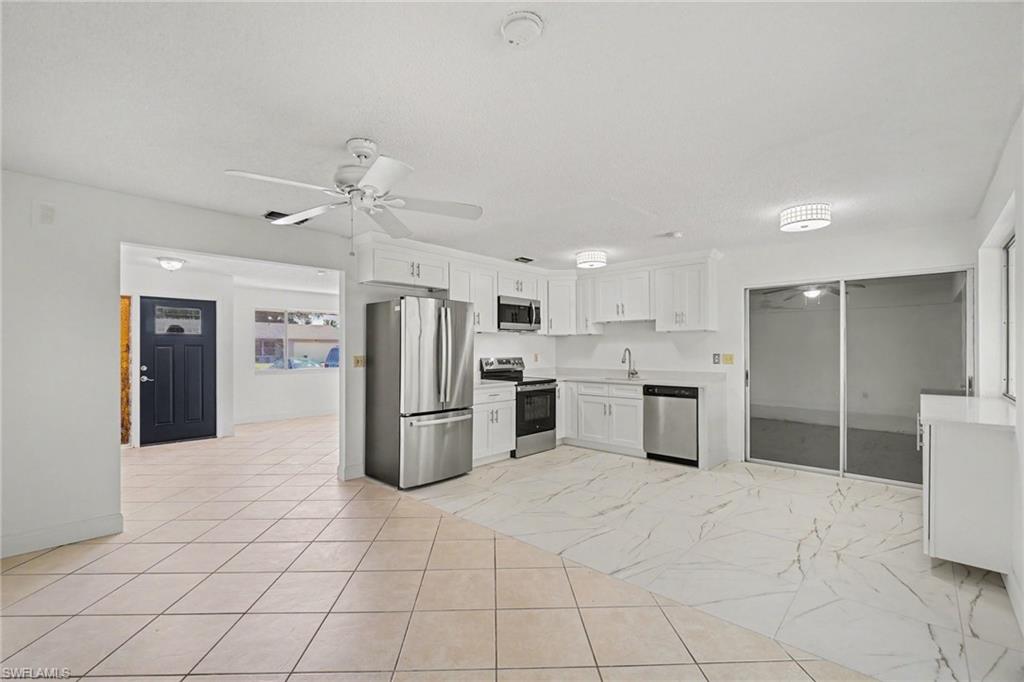 Open-concept living area featuring a kitchen with white cabinetry, stainless steel appliances, and light-toned countertops