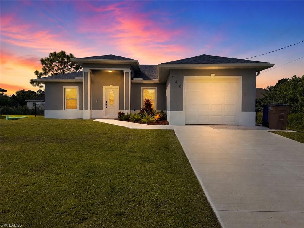 Stucco exterior with a blue and white color scheme, a white garage door, a concrete driveway, and a landscaped front entrance
