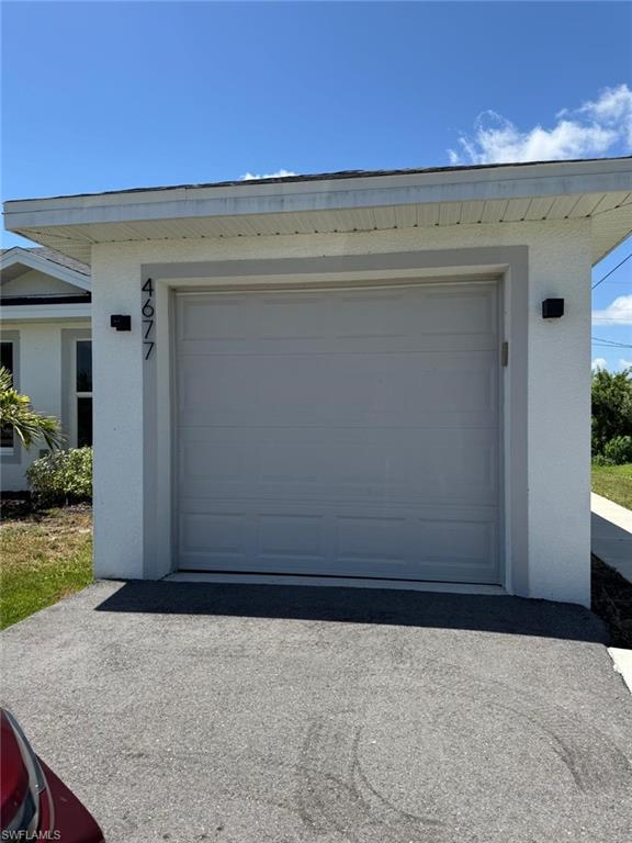 Attached garage with a panel door, exterior wall sconces, and a paved driveway