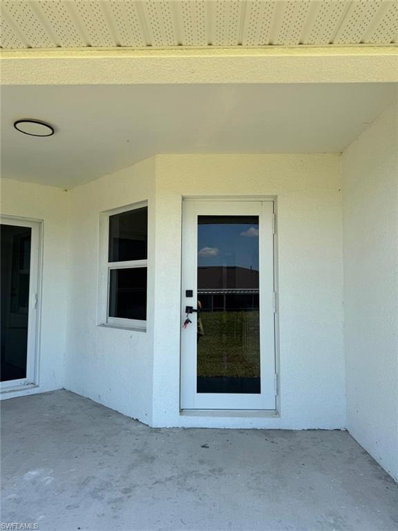 Expansive concrete patio featuring a glass-paneled door, corner window, and overhead lighting