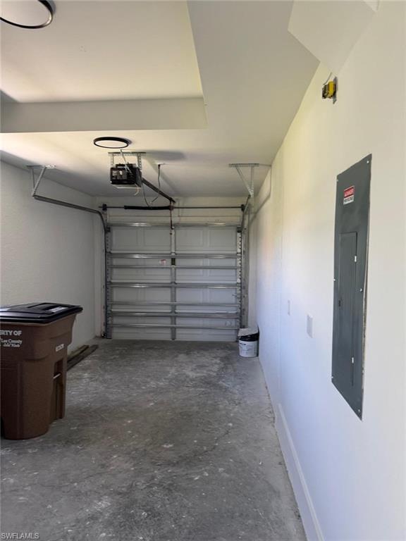 Attached garage with a sectional garage door, concrete flooring, and a wall-mounted electrical panel