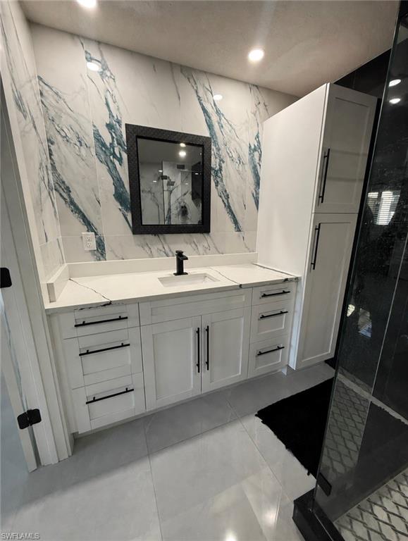 White shaker-style vanity with a single basin sink, white stone-finish countertop, and black hardware