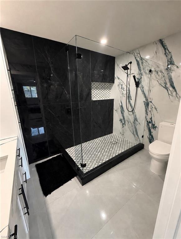 Glass-enclosed shower with black and white veined tile walls, geometric mosaic shower floor, and matte black shower fixtures