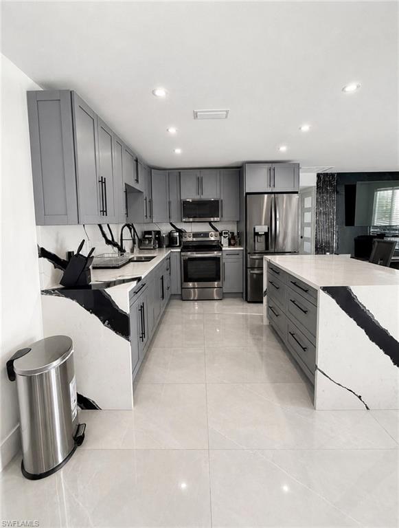 Modern kitchen featuring light gray cabinetry, stainless steel appliances, a large center island, distinctively veined countertops, and recessed lighting