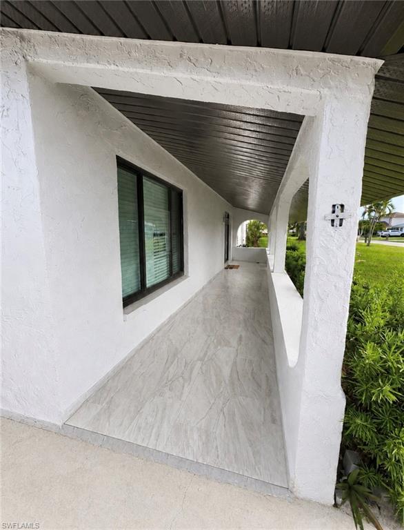 Covered entry featuring a textured white stucco exterior, dark soffit, and light-toned tile flooring
