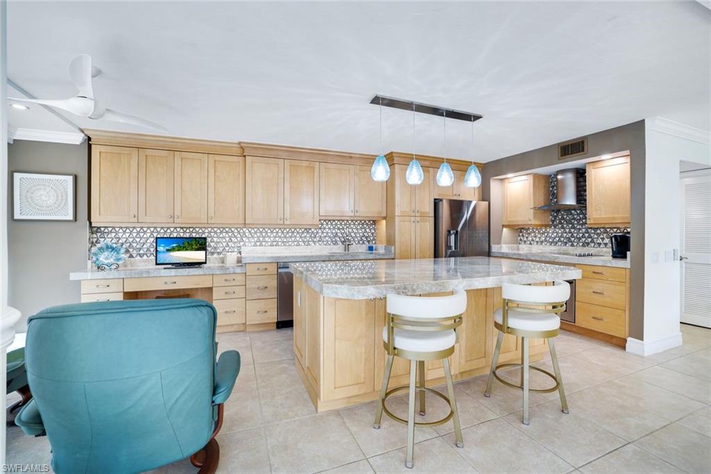 Kitchen featuring stainless steel fridge, decorative light fixtures, backsplash, wall chimney range hood, and a center island