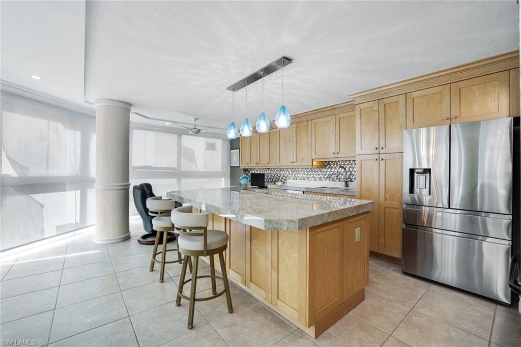 Kitchen featuring stainless steel fridge, decorative light fixtures, backsplash, a center island, and light stone countertops