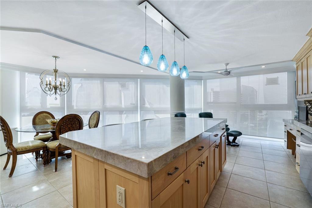 Kitchen featuring ceiling fan with notable chandelier, light tile patterned floors, a kitchen island, and decorative light fixtures
