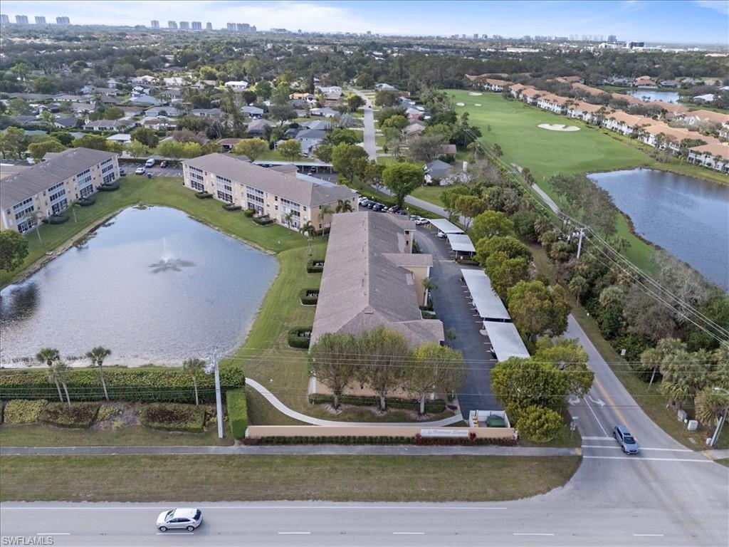 Lush landscaping surrounds the property, featuring a large pond with a fountain, covered parking structures, and manicured green spaces