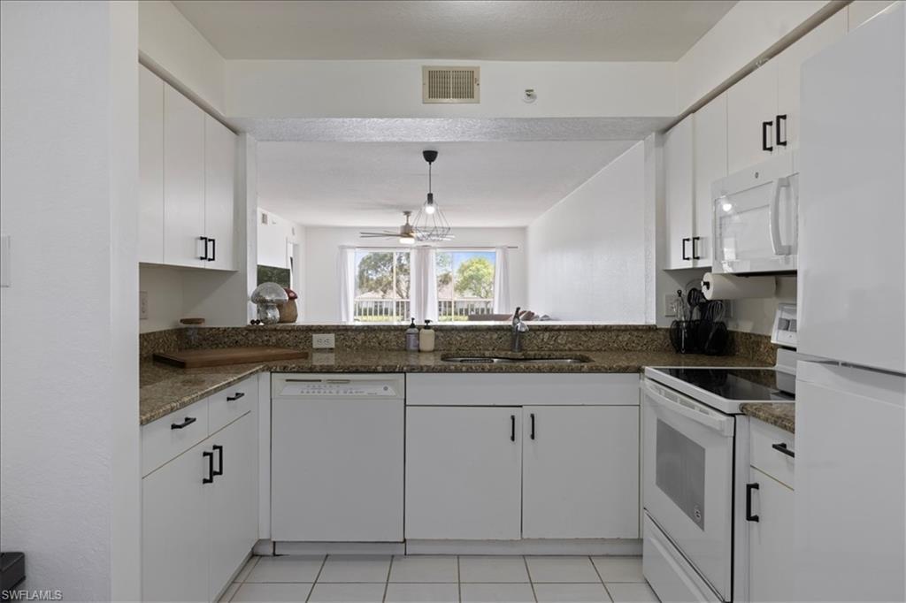 White cabinetry with black hardware, granite countertops, white tile flooring, built-in microwave, and a pass-through opening