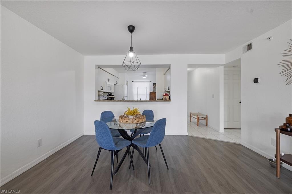 Wood-finish flooring throughout, a geometric pendant light fixture, and a kitchen pass-through with a breakfast bar