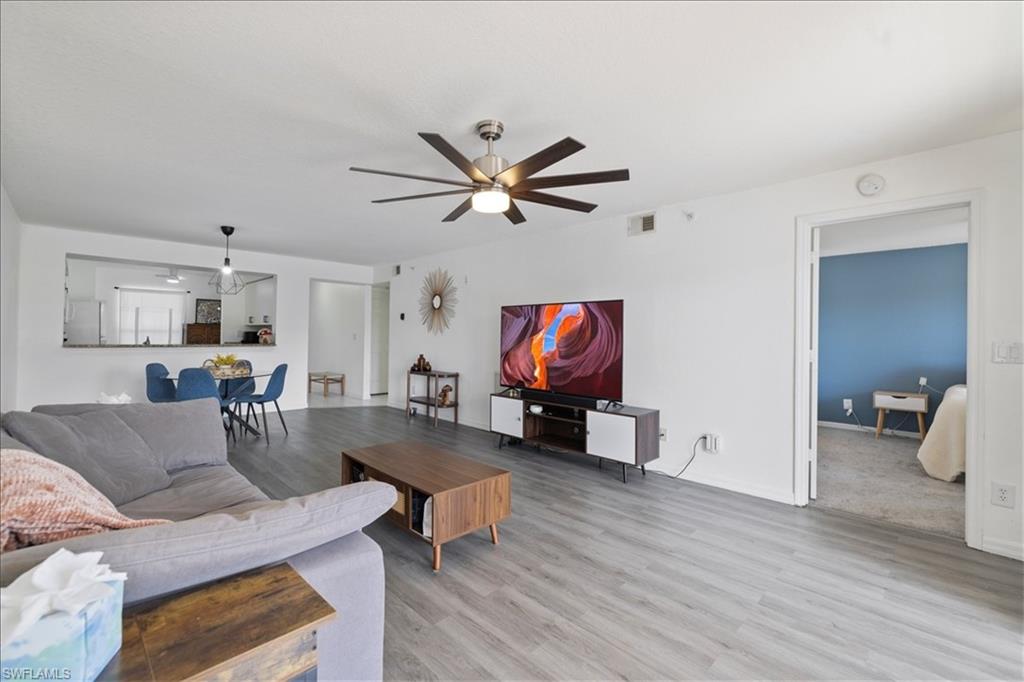 Open-concept living area featuring wood-finish flooring, a ceiling fan with integrated lighting, and a pass-through window to the dining space