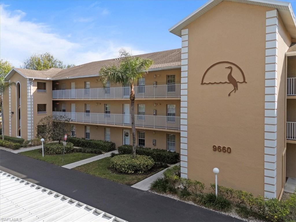 Multi-story building featuring exterior balconies with white railings, a stucco finish, and manicured landscaping