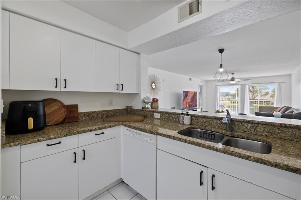 White cabinetry with matte black hardware, dual basin stainless steel sink, granite countertops, and white tile flooring