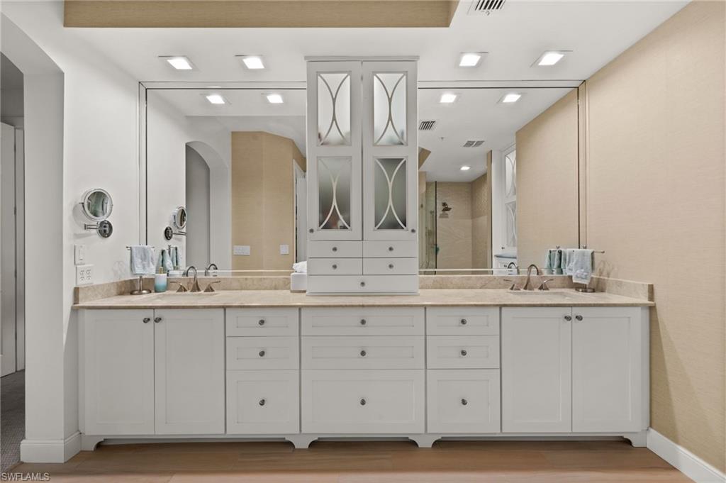 Dual sink vanity with stone countertop, extensive white cabinetry, integrated storage tower, and recessed lighting